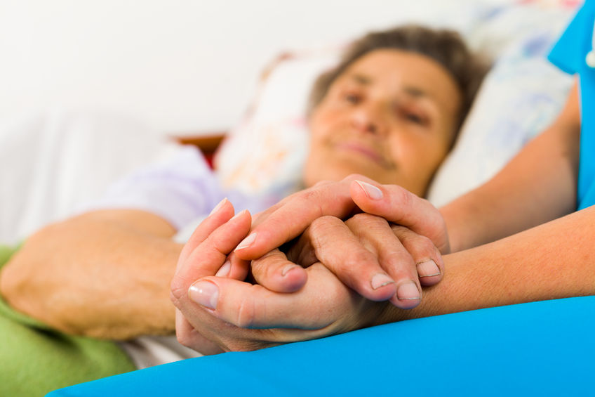 55422020 – caring nurse holding kind elderly lady’s hands in bed.